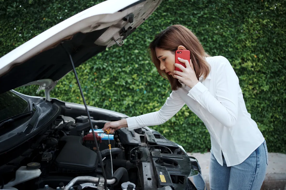 Woman calling a breakdown recovery service on her mobile after her car broke down